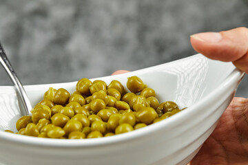Hand holding a bowl of boiled green peas on a marble background