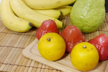 Tropical fruits background. Apple, banana and guava on bamboo table. Oranges and wax apples on wooden plate. Concept for harvest, eating, vitamins and health.
