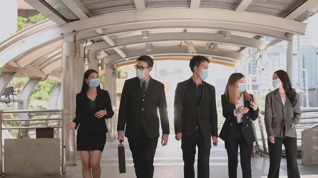 Group Of Asian Business People In Suit And Wearing Hygiene Face Mask To Protection Pandemic Of Coronavirus Or Covid 19 Walking Talking Together On Overpass In City. New Normal And Teamwork Concept