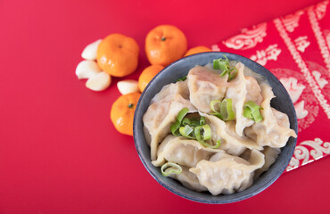 A bowl of dumplings on a red background with a few garlic petals and red packets and a few oranges