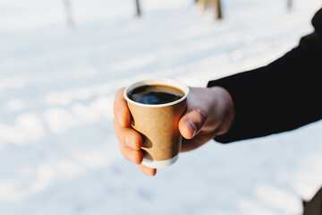 The guy holds a paper cup of coffee in his hand in the snowy forest