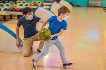 Fototapeta na wymiar Father and son playing bowling with medical masks during COVID-19 coronavirus in bowling club