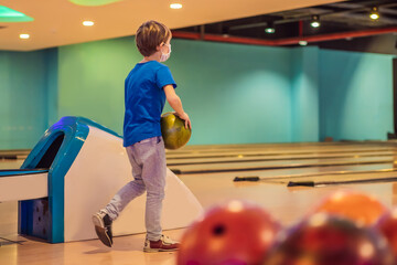 Boy playing bowling with medical masks during COVID-19 coronavirus in bowling club