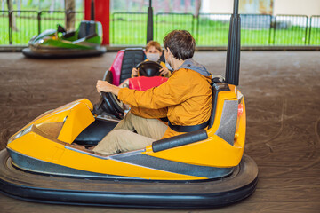 Dad and son wearing a medical mask during COVID-19 coronavirus having a ride in the bumper car at the amusement park