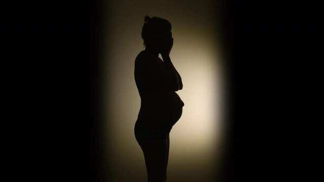 SILHOUETTE VIGNETTE of a heavily pregnant woman suddenly laughing