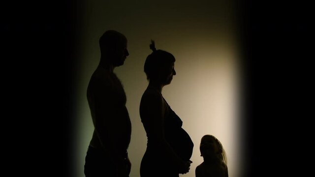 SILHOUETTE VIGNETTE of family, dad, very pregnant mum and a cheeky toddler