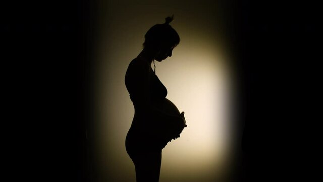 VIGNETTE SILHOUETTE, A heavily pregnant woman strokes her big belly