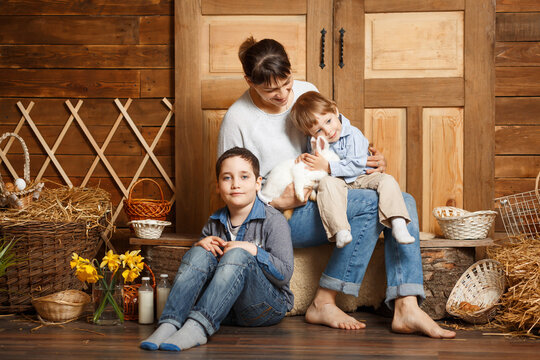 Excited Little Boys And Female Spending Easter Day At Family Farm. Family In Rural Wooden Interior With Flowers In Studio. Mother And Sons In The Village. Happy Easter.Easter Preparations. Holiday.