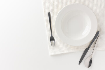 A white plate on a white table with cutlery placed There is no food on the plate. Household equipment