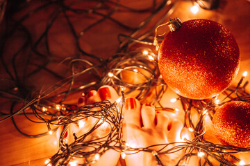 Fototapeta na wymiar Woman naked feet with red nails lying on warm yellow Christmas lights 