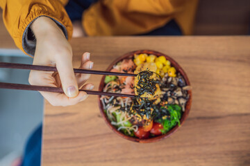 Woman eating Raw Organic Poke Bowl with Rice and Veggies close-up on the table. Top view from above...