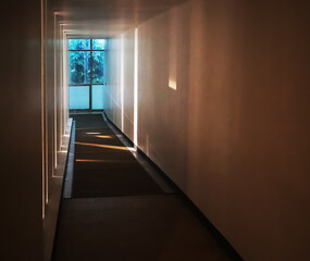 Perspective interior image of long corridor hall way ramp in the room connect to the lower level floor with strip of light through the opening wall and transparent window clear view of outdoor nature.