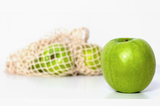 Green apples in eco mesh bag on white kitchen table. Market shopping. Food and Environment concept. Zero waste. Close up. Banner.