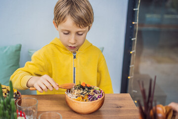 Boy eating Raw Organic Poke Bowl with Rice and Veggies close-up on the table. Top view from above horizontal