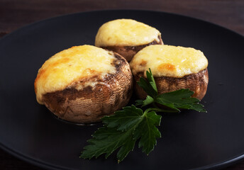 Baked mushrooms stuffed with cheese and herbs on a black plate. wooden background.