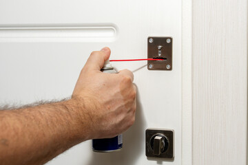 a man fixing a door lock with a lubricant - obrazy, fototapety, plakaty
