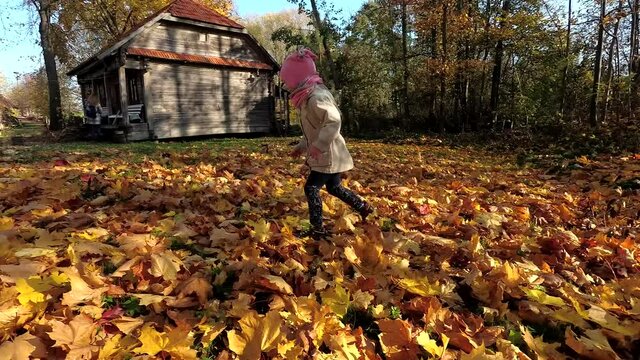 Little girl daughter run colorful leaves and mother with son in background