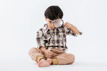 Child holding magnifying glass on white background. Boy with a magnifying glass in studio. Positive...