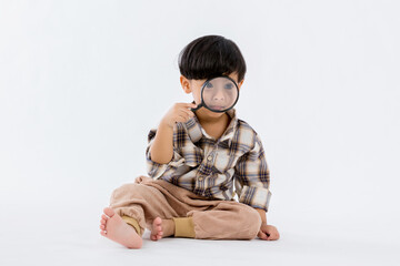Child holding magnifying glass on white background. Boy with a magnifying glass in studio. Positive curious boy in casual wear looking at through magnifier 