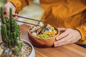 Man eating Raw Organic Poke Bowl with Rice and Veggies close-up on the table. Top view from above horizontal