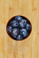 Garden plums in a bowl on wooden background