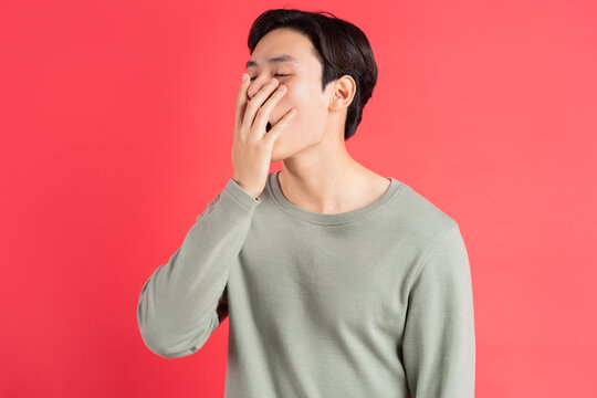 A photo of a handsome Asian man yawning with his hand over his mouth