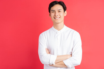 A photo of a handsome Asian man standing with his arms crossed on a red background