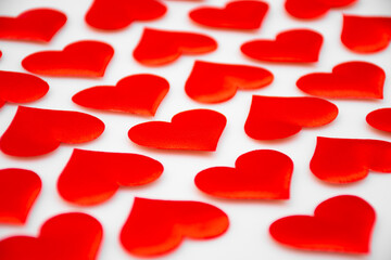 Lots of textured red hearts lie diagonally behind each other on a white background, selective focus: Valentine's day background, seamless heart pattern