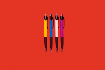 four colored pens lying on a red background