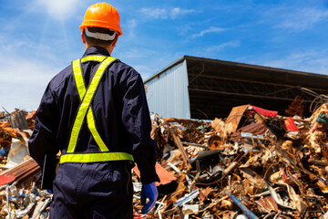 Engineer working at a pile of scrap metal recycling and recycling industry. Engineer wearing protective equipment and holding computer tablet and looking at scrap metal pile.