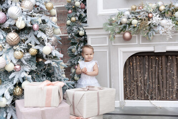Fototapeta na wymiar Happy Little baby girl posing among Christmas decorations and Christmas tree in a cosy interior with a fireplace