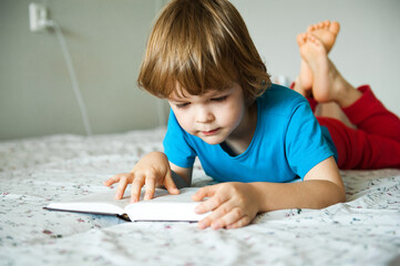Little boy lying on the bed and reading a book.