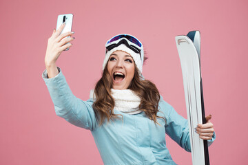 fun skier takes a selfie on her smartphone. A young woman with ski equipment in a jacket and hat,