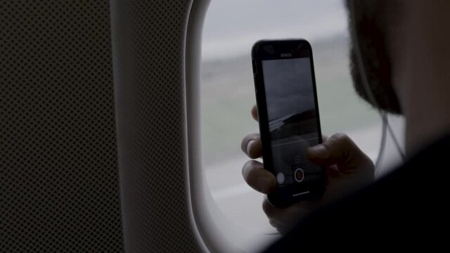Unrecognizable Caucasian man taking picture with smartphone from airplane window