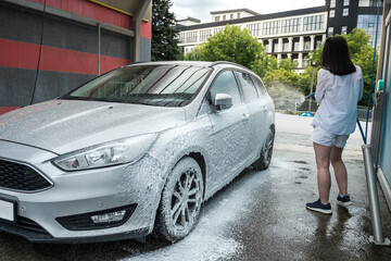 Ukrainian woman  with foam water gun cleans her car in service