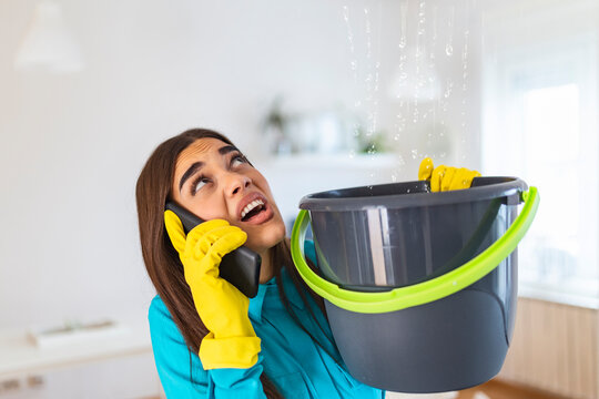 Worried Young woman Calling Plumber While Leakage Water Falling Into Bucket At Home