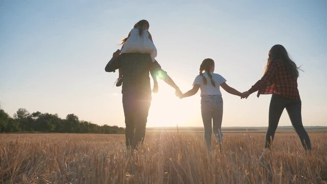 Happy family park at sunset in evening.Mom,dad,child are happy walking in sun.Family walk along field holding hands. Parents hold their children by hands at sunset park.Friendly cute family together