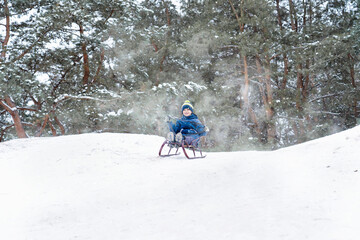 Boy sledding in a snowy forest. Outdoor winter fun for Christmas vacation.