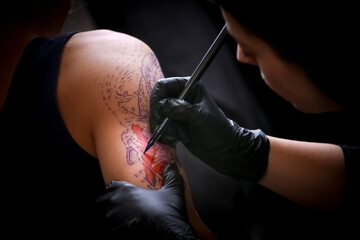 Female tattoo artist making tattoo on a men’s arm