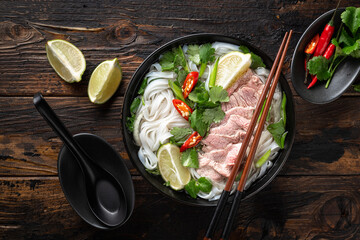 Pho Bo vietnamese soup with beef and noodles on a wooden background, top view - obrazy, fototapety, plakaty