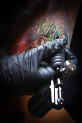 Naklejka na ściany i meble Female tattoo artist making tattoo on a men’s arm