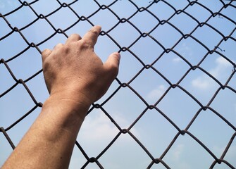 Human hand holding jail, blue sky background.
