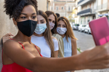 Happy multiracial friends taking a selfie and wearing protective face masks, concept of health care...
