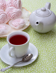 A white mug with a teapot next to a marshmallow. Selective focus.