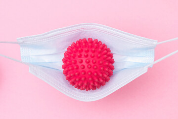 A red ball with spikes coronavirus swinging in a medical mask like in a hammock or swing.