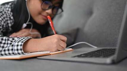Close up view of Asian girl student during online courses on laptop computer while lying on sofa at home.