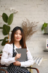 Fototapeta premium Attractive coffee shop entrepreneur holding digital tablet and stylus pen sitting at her cafe.