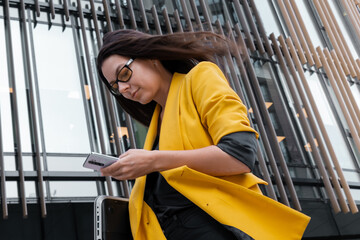 businesswoman in a bright yellow jacket uses a smartphone,