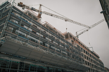 Modern city block construction in the city center, visible cranes and concrete facade on a gray day.