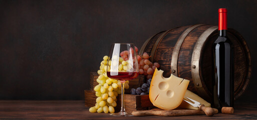 Wine bottle, grapes, glass of red wine and old barrel